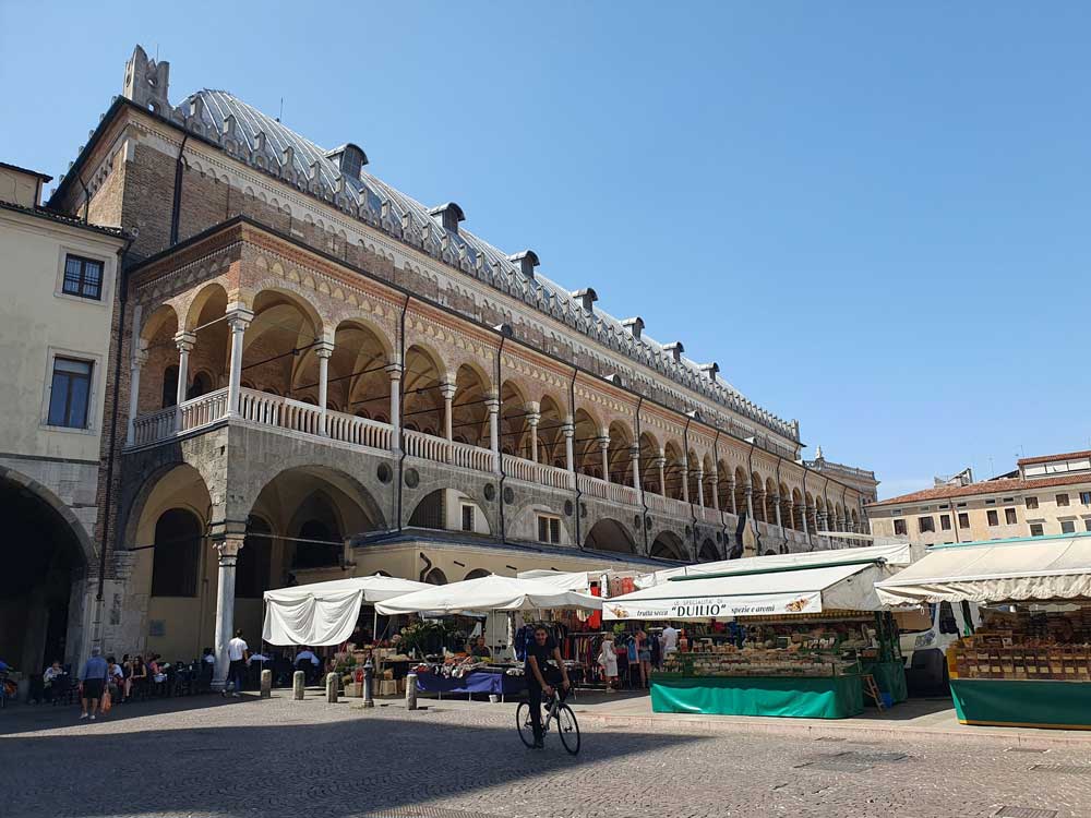 View of Palazzo della Ragione, Padua, with market stalls and a cyclist